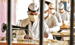 Inmates learning a trade. Inmates using sewing machine while wearing a hat and face-mask. Photo Credit: PTI