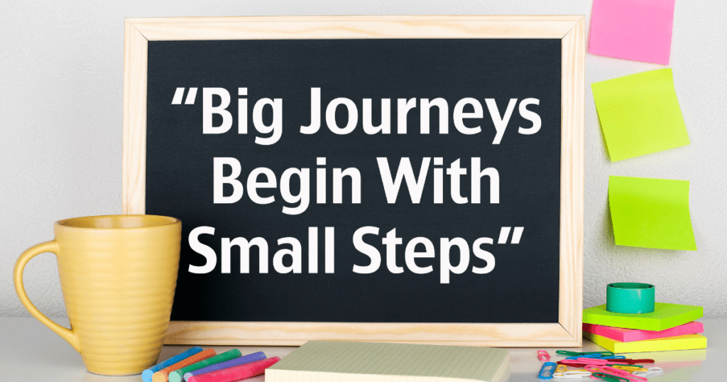 A written quote on a blackboard surrounded with a coffee mug and post-its that says, "Big journeys begin with small steps."