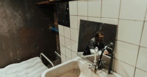 A man thinking in a jail cell. This reflection is showcased on the mirror which is right under the sink