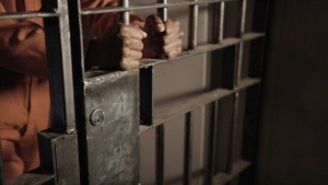 An incarcerated person holding the bars of jail from a prison cell. 